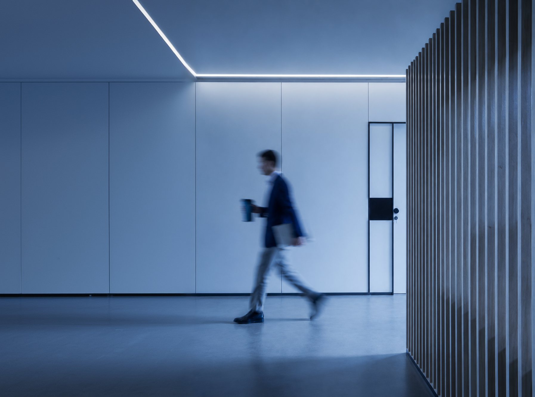 Blurred figure walking through a modern office corridor with cool lighting.